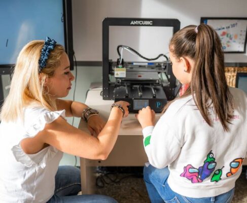 Una docent assenyala la pantalla d'una impressora 3D, davant la mirada atenta d'una seva alumna.