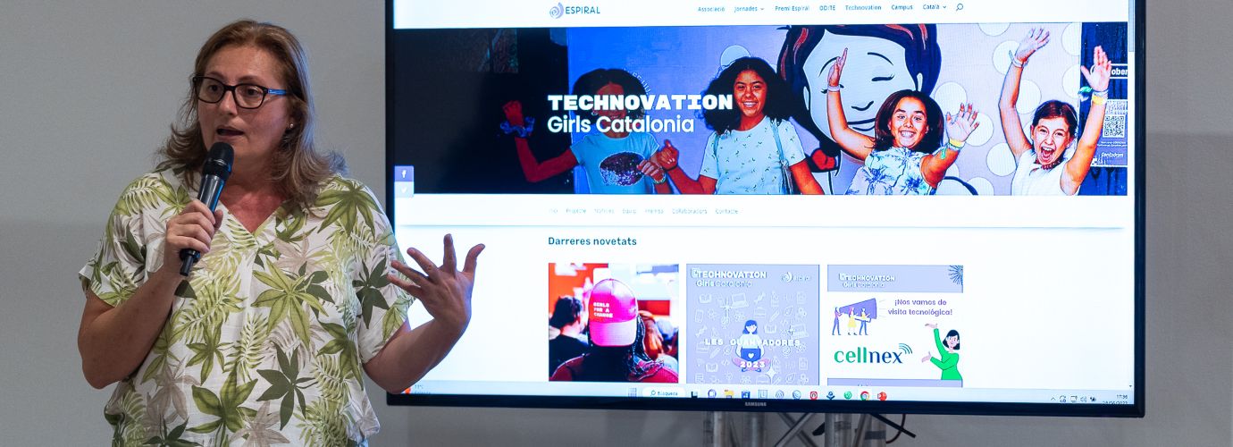 Apareix la Rosa Prats en un primer pla, fent una intervenció sobre el projecte Technovation Girls, amb una pantalla al darrere on està projectada la web del projecte.