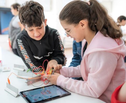 Apareixen una nena i un nen jugant amb un placa electrònica i una tauleta, en el que suposem és una classe de pensament computacional a una aula ordinària de Catalunya.
