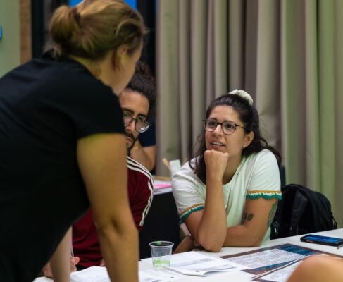 Apareix una mestra escoltant atentament la indicació d'una altra, enmig d'un taller.