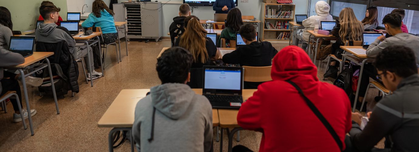 Apareixen un grup d'estudiants de secundària escoltant una classe magistral, davant dels seus ordinadors.